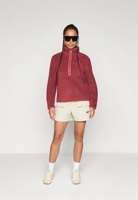 Fleece pullover in dark red with a half zipper and textured design. Paired with light beige shorts featuring front pockets.