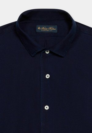 Ciemnogranatowa koszula na guziki z klasycznym kołnierzykiem, trzema widocznymi białymi guzikami oraz metką Brooks Brothers wewnątrz kołnierzyka.