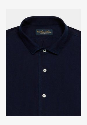 Dunkelblaues Hemd zum Knöpfen mit klassischem Kragen, drei sichtbaren weißen Knöpfen und einem Brooks Brothers-Label auf der Innenseite des Kragens.