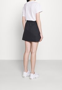 Czarna casualowa spódnica z elastycznym pasem i boczną kieszenią, w połączeniu z białą koszulką i białymi trampkami, widok z tyłu.