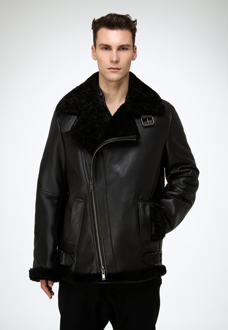 Schwarze Lederjacke mit großem Lammfellkragen, Reißverschluss, Seitentaschen und Schnallenakzenten an Ärmeln und Saum.