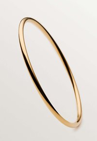 Brazalete de metal color dorado con un perfil liso y redondeado, y un acabado pulido que enfatiza su diseño minimalista y sin costuras.