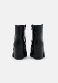 Schwarze Leder-Stiefeletten mit einem hohen gerippten Absatz. Sie verfügen über einen Reißverschluss und eine glatte Oberfläche, die für einen enganliegenden Look gestaltet ist.