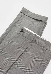 Pantalons sur mesure à carreaux gris avec un tissu texturé. Dotés d'une fermeture à bouton et de plis soignés, pliés soigneusement sur un fond clair.