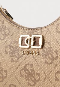 Geantă texturată aurie și maro cu închidere cu fermoar, având un accent proeminent cu logo auriu și model în relief pe material bej.