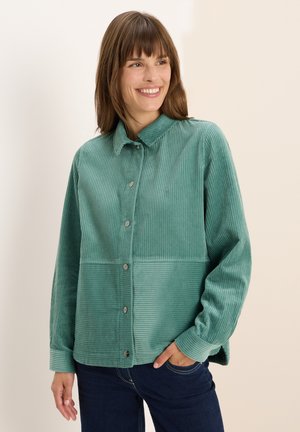 Veste chemise en velours côtelé vert d'eau avec un devant à boutons, un col et une texture côtelée. Présente un panneau horizontal contrastant.