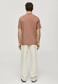 Camiseta de manga corta a rayas marrón y crema con cuello redondo, combinada con pantalones ancho crema. Vista trasera, sin logotipos visibles.