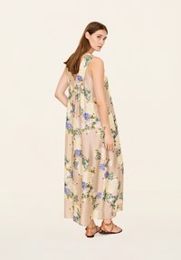Blumiges Maxikleid aus beige farbenem Stoff mit blauen und gelben Blumen. Es hat einen lockeren Schnitt, ein offenes Rücken-Design und dünne Träger.