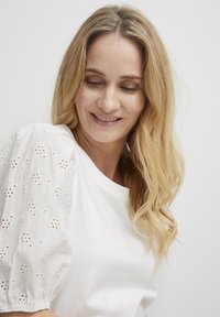 Hvid T-shirt med puffede, broderede hvideærmer, der har blomsterudskæringer. Glat stofstruktur, afslappet pasform, rund halsudskæring.