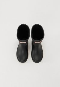 Bottes de cheville en caoutchouc noir avec une texture lisse, bout rond et étiquette logo rouge et blanc à l'avant. Design minimaliste.