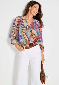 Bunte gemusterte Bluse mit geometrischen Designs in Rot, Blau und Braun, mit V-Ausschnitt, Dreiviertelärmeln und leichtem Stoff.