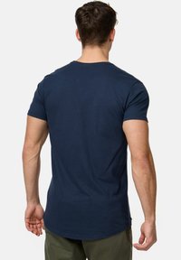 Mørkeblå bomulds t-shirt med korte ærmer, rund hals og en lidt længere bagkant. Glat tekstur, minimalistisk design.