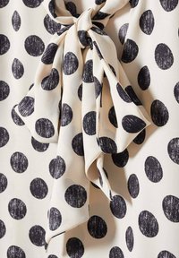 Tissu crème avec des pois noirs irréguliers, agrémenté d'un nœud noué.