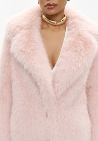 Blød lyserød kunstpelsjakke med dyb V-udskæring, brede kraver og glitrende gylden choker. Tekstureret med en fluffy, luksuriøs finish.