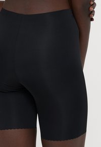 Sorte sømløse shapewear-shorts med en glatt tekstur og scalloped kant, designet for komfort og dekning. Slutter rett over midt-thigh.