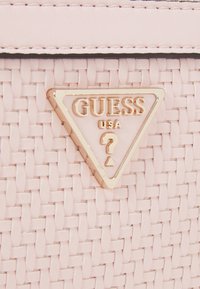 Różowa pleciona torebka z złotym logo w kształcie trójkąta z napisem "GUESS USA" oraz znakiem zapytania. Gładkie skórzane akcenty u góry.