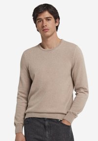 Beige crewneck-tröja i mjukt, strukturerat tyg. Har ribbstickade muddar och fåll, med en smal passform och minimalistisk design. Bärs med mörka jeans.