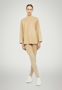 Beige synthetic top with three-quarter sleeves paired with light gold, sparkly leggings and white athletic shoes. Smooth textures, minimal design.