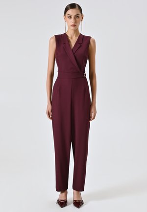 Jumpsuit senza maniche color borgogna con design a scollo a V avvolto, vita stretta e pantaloni larghi, dotato di una grande fibbia circolare.