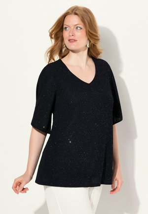 Top blu navy a V con maniche corte, caratterizzato da una texture scintillante e un fit morbido. Abbinato a pantaloni bianchi.