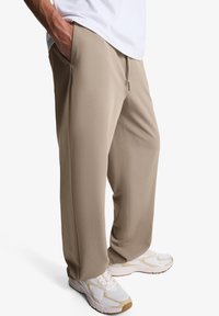 Pantaloni de jogging bej, ușori, cu croială dreaptă, talie elastică și buzunare. Asortați cu teneși albi cu accente bej.