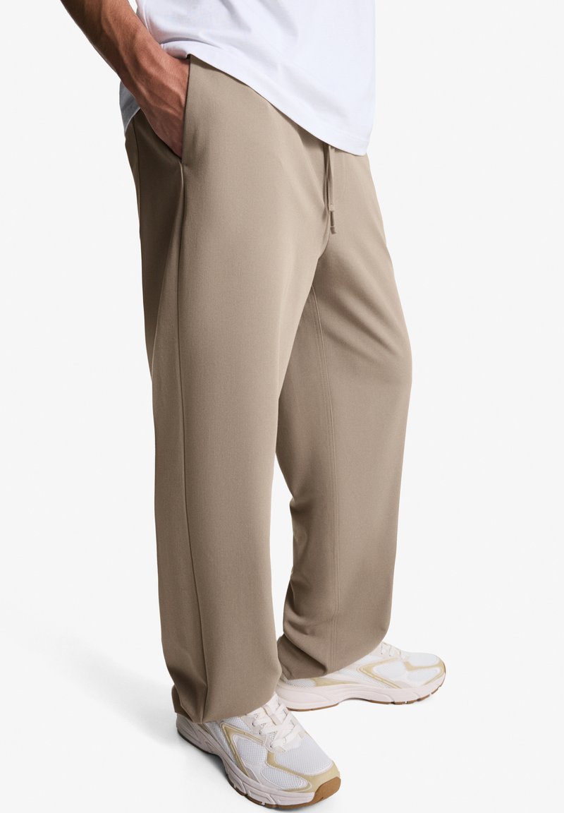 Pantaloni de jogging bej, ușori, cu croială dreaptă, talie elastică și buzunare. Asortați cu teneși albi cu accente bej.