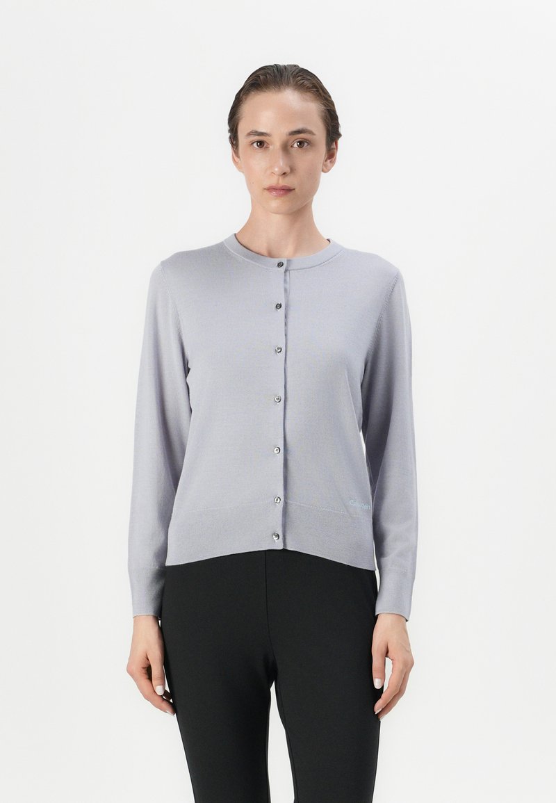 Cardigan malha lilás claro com decote redondo e mangas longas, apresentando uma frente com botões e uma textura suave. Os acabamentos incluem botões prateados.