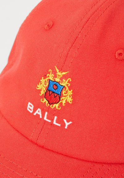 Casquette de baseball en coton rouge ornée d'un blason brodé avec des éléments bleus et rouges et des accents dorés. Le mot "BALLY" est cousu en blanc.