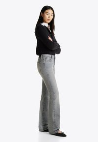 Lahtised hallid teksad, millel on kulunud viimistlus, tekstureeritud denim, viie tasku disain ja mustad baleriinakingad. Modell kannab musta sviitrit ja valget asja.