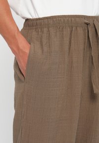 Lightweight brown pants with an elastic waistband and drawstring, featuring a textured fabric and side pockets.