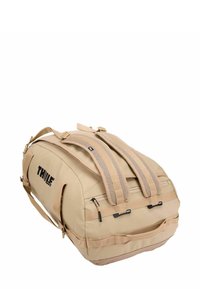 Sac de voyage beige avec deux bretelles ajustables et rembourrées, poche zippée et grande marque. Tissu durable avec une texture lisse.