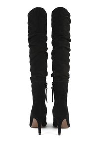 Botas de gamuza negras altas y sueltas con cremalleras traseras y tacones altos delgados, mostradas desde la parte trasera sobre un fondo blanco.
