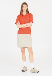 Röd kortärmad polo med knappslå, parat med en beige knälång kjol med sidoficka, bärs med beige sneakers.