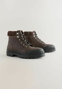 Braune Leder-Stiefeletten mit Wildlederakzenten, Schnürung an der Vorderseite, seitlichem Reißverschluss und einer robusten Gummisohle mit einer Profilstruktur.