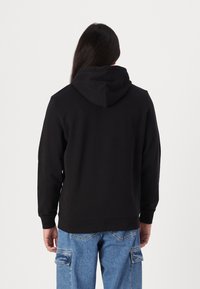 Sort hoodie med en løs pasform, der har en blød tekstur, kængurulomme og snøre i hætten. Bæres med lyseblå cargo jeans.
