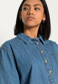 Denimskjorte i lys blå, med spiss krage, knappelukking foran og brystlomme. Materialet har tekstur med en klassisk passform.