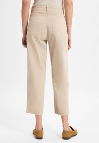 Beige cropped broek met een soepele textuur, voorzien van twee achterzakken en een rechtzittend ontwerp, gecombineerd met bruine instapschoenen.