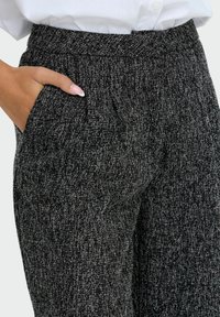 Pantaloni neri e bianchi con texture, cintura ampia e tasche laterali, caratterizzati da un delicato motivo screziato in tutto il tessuto.