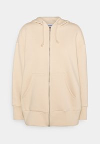 Sweat à capuche beige à fermeture éclair avec capuche à cordon de serrage, grandes poches frontales, poignets côtelés et coupe ample. Fabriqué en tissu doux et confortable.