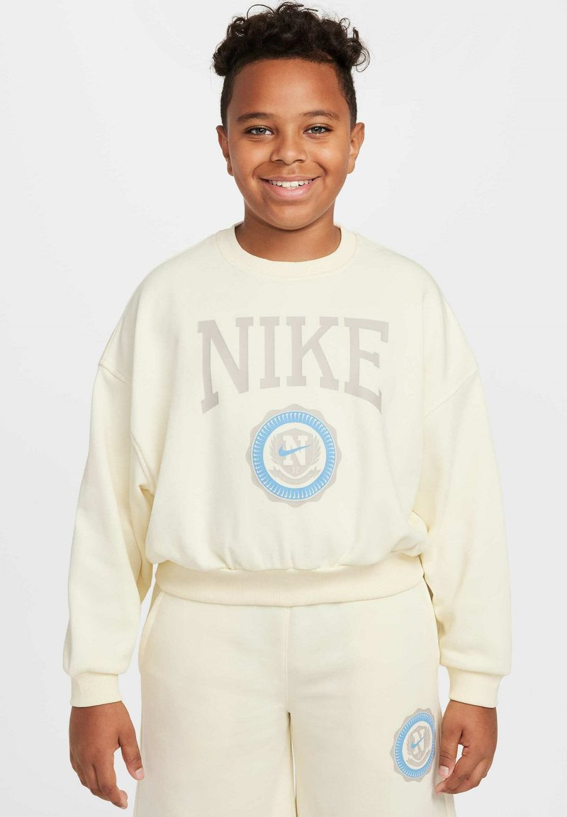 Sudadera de gran tamaño en crema claro con la palabra "NIKE" en gris y un acento de logo circular azul. Parte inferior a juego, puños ribeteados y cintura.