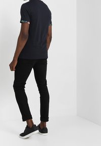 Námořnické tričko s květinovým vzorem na manžetách, doplněné černými slim-fit džíny a černými teniskami. Pohled z zad zobrazuje jednoduchý design.