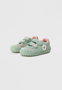 Green suede sneakers with pink accents, double Velcro straps, flower appliqué, textured sole, and decorative stitching on the sides.