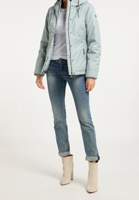 Chaqueta acolchada azul claro con capucha, camiseta blanca debajo, vaqueros con los puños remangados y botines beige con tacón cuadrado.