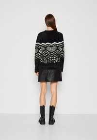 Schwarzer, flauschiger Pullover mit weißen geometrischen und Tiermustern, kombiniert mit einem schwarzen Lederrock und knielangen schwarzen Stiefeln.
