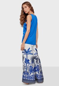Blue sleeveless top paired with wide-legged pants featuring a white base and bold blue tropical print, including palms and birds. Smooth texture.