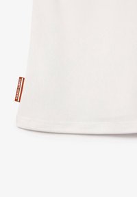 Vêtement en tissu blanc avec une texture lisse, équipé d'une étiquette rouge sur le côté avec le texte "ROLAND GARROS" en blanc.