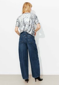 Haut en sequins argentés à manches courtes associé à un jean large bleu foncé avec poches arrière et chaussures à talons noires.