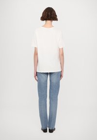 Weißes T-Shirt mit kurzen Ärmeln und lockerer Passform, kombiniert mit hellblauen, geraden Jeans, von hinten betrachtet. Glatte Textur, minimales Design.