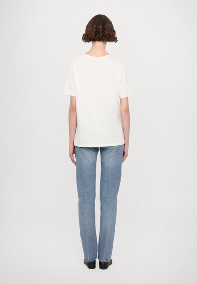 Hvit kortermet t-skjorte med en avslappet passform, kombinert med lyse straight-leg jeans, sett fra baksiden. Glatt tekstur, minimalistisk design.