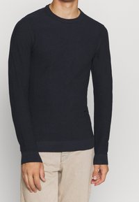 Mörkblå långärmad stickad tröja med ett texturerat mönster, ribbade ärmslut och nederkant. Tillverkad av mjukt material, figursydd vid midjan.